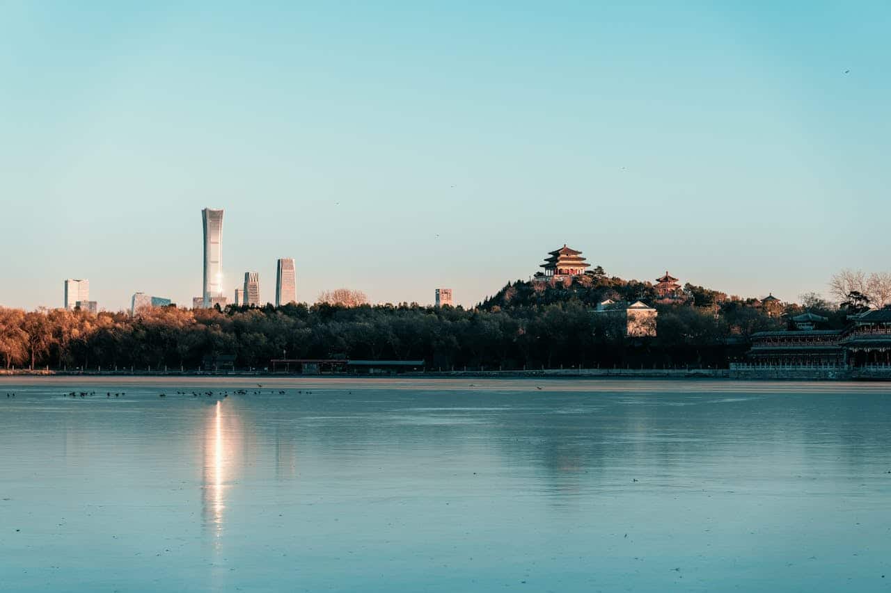 Beijing's modern skyline and historic Beihai Park white pagoda reflected in a calm lake at dusk, old and new architecture side by side.
