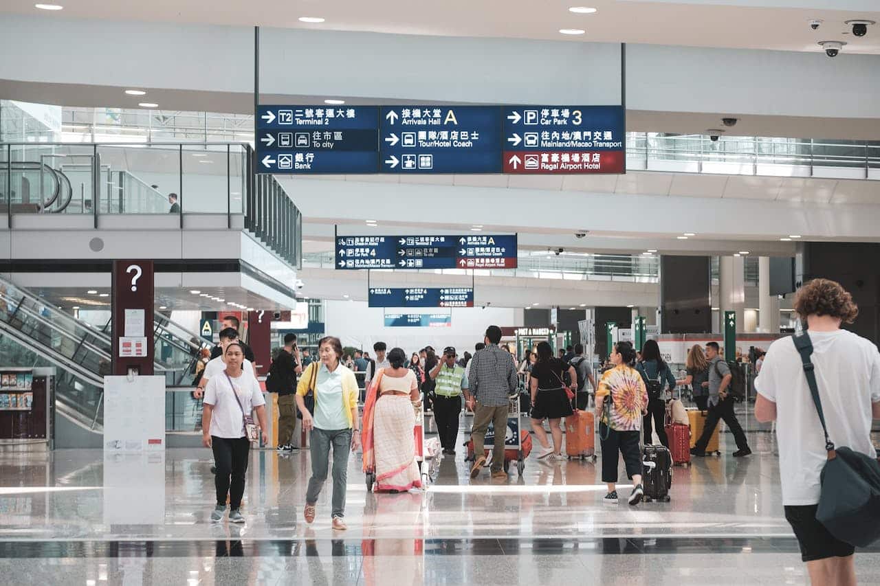 International travelers walking through Hong Kong International Airport terminal with Chinese and English directional signs