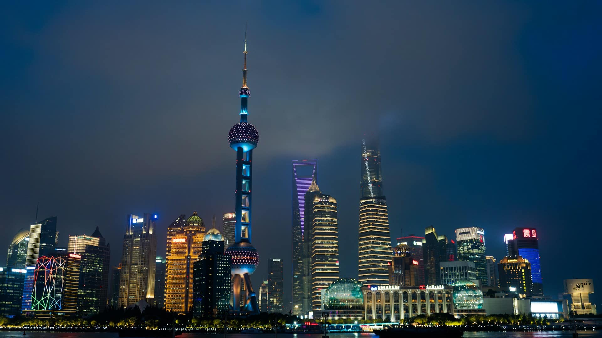 Shanghai Bund skyline at night with Oriental Pearl Tower and Pudong skyscrapers reflecting on the Huangpu River