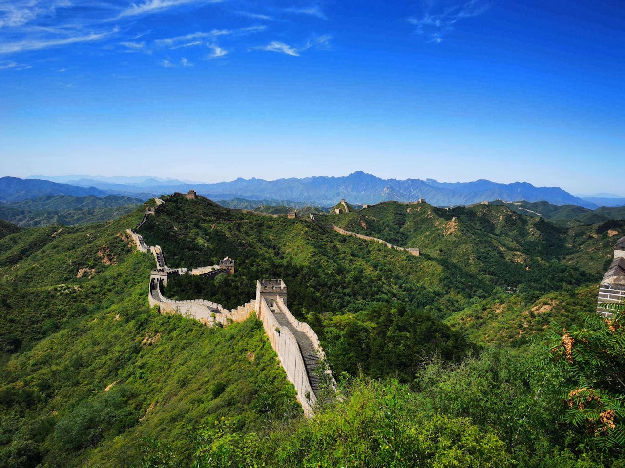 Great Wall of China stretching across lush green mountain ridges under a clear blue sky, Jinshanling section, Beijing