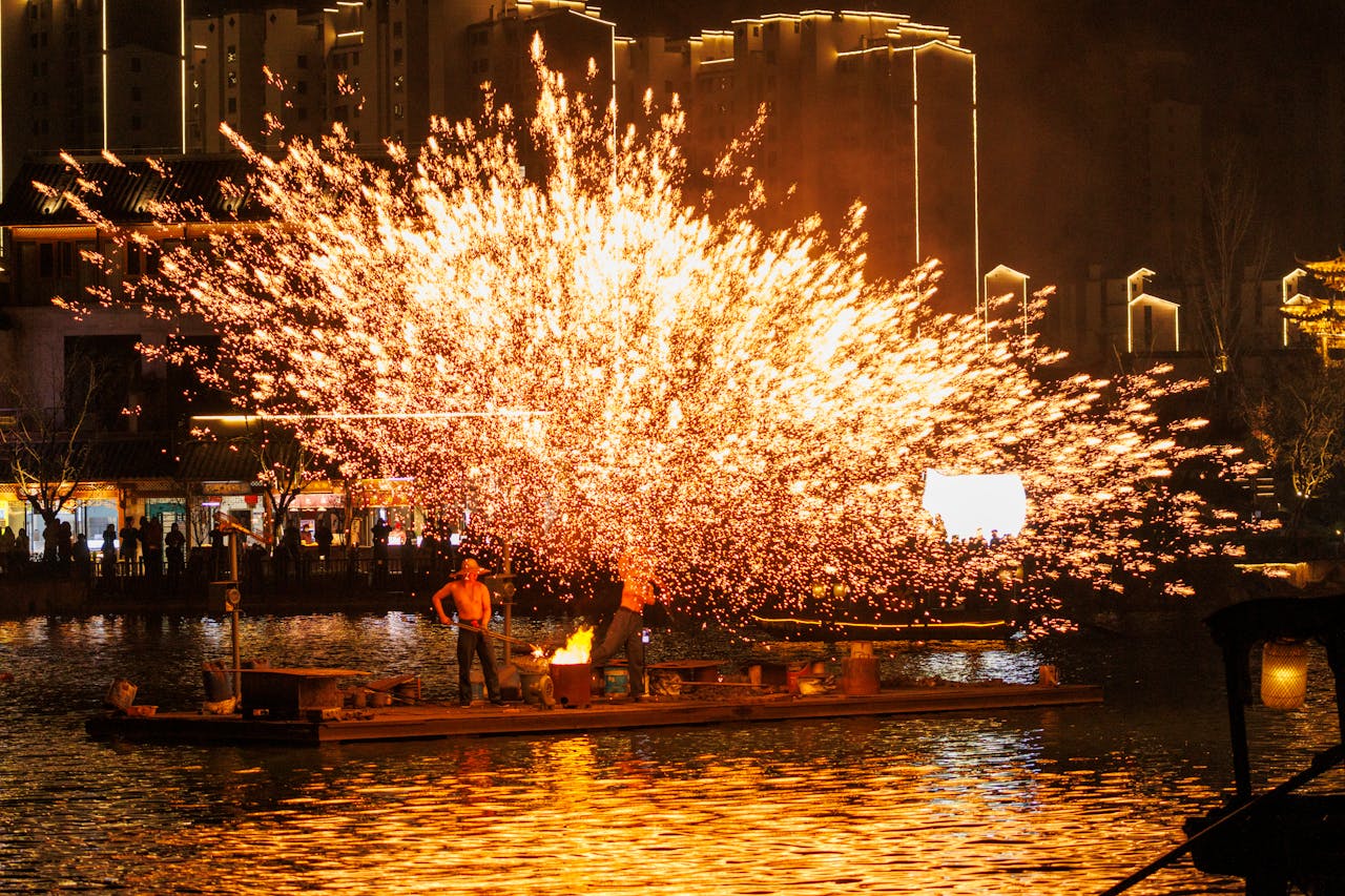 Traditional Chinese blacksmith performing Da Tie Hua (iron flower) ritual, throwing molten iron into air creating spectacular golden sparks shower against dark night sky.