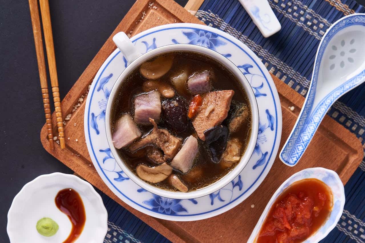 A bowl of traditional Chinese TCM soup with mushrooms and tofu served on a wooden tray, representing the herbal food culture foreigners can experience when traveling in China.