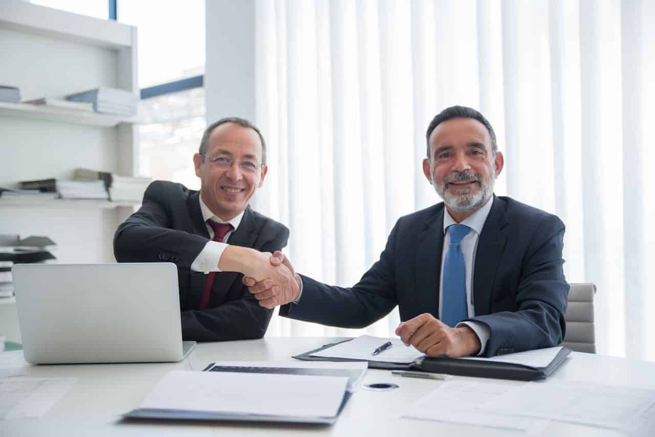 Two businessmen shaking hands to close a supplier deal in a professional office setting