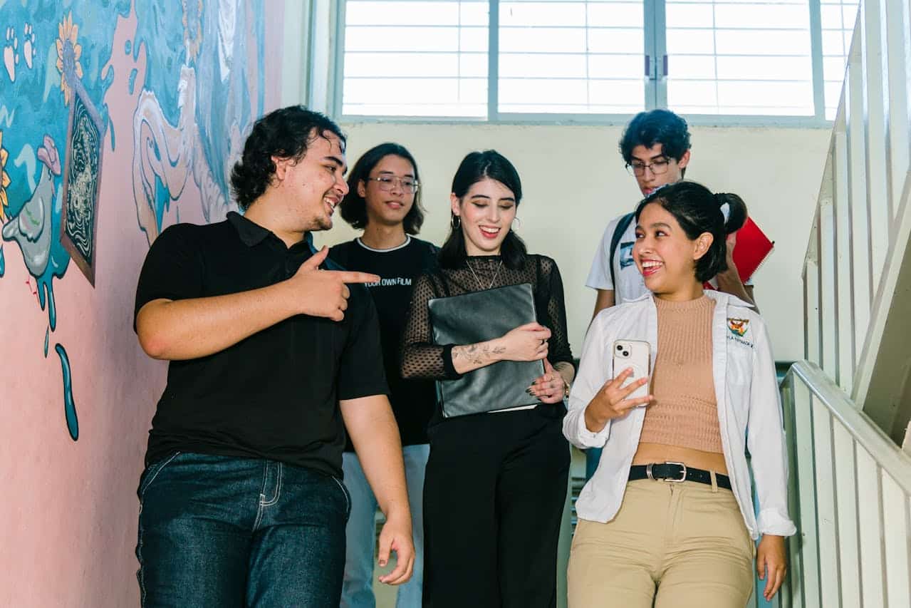 International students walking and talking on university campus stairwell, carrying laptops and notebooks