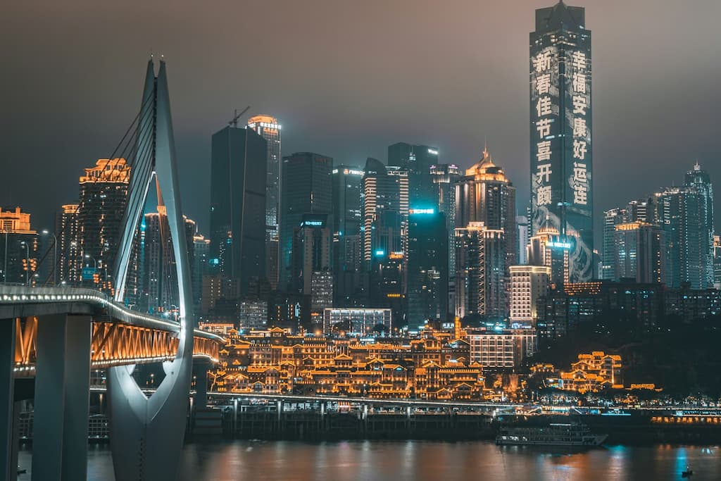 Chongqing Municipality night skyline showing stacked illuminated highways and high-rise towers rising up the hillside above the Yangtze River
