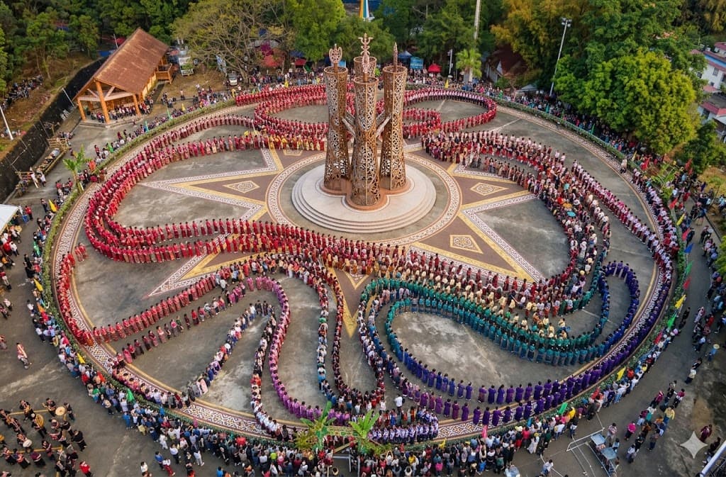Aerial view of thousands of Jingpo participants in black ceremonial costumes dancing in spiral formation around Munao Shidong pillars at Munao Zongge festival, Dehong Yunnan
