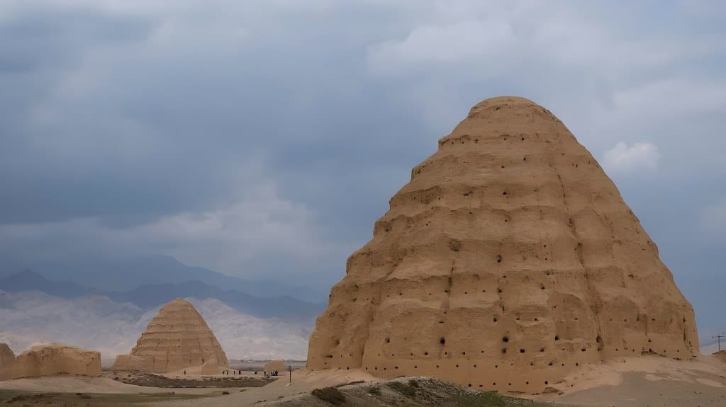 Large beehive-shaped earthen mausoleums of the Western Xia Dynasty standing in a desert landscape against the hazy Helan Mountains under a cloudy sky in Ningxia.