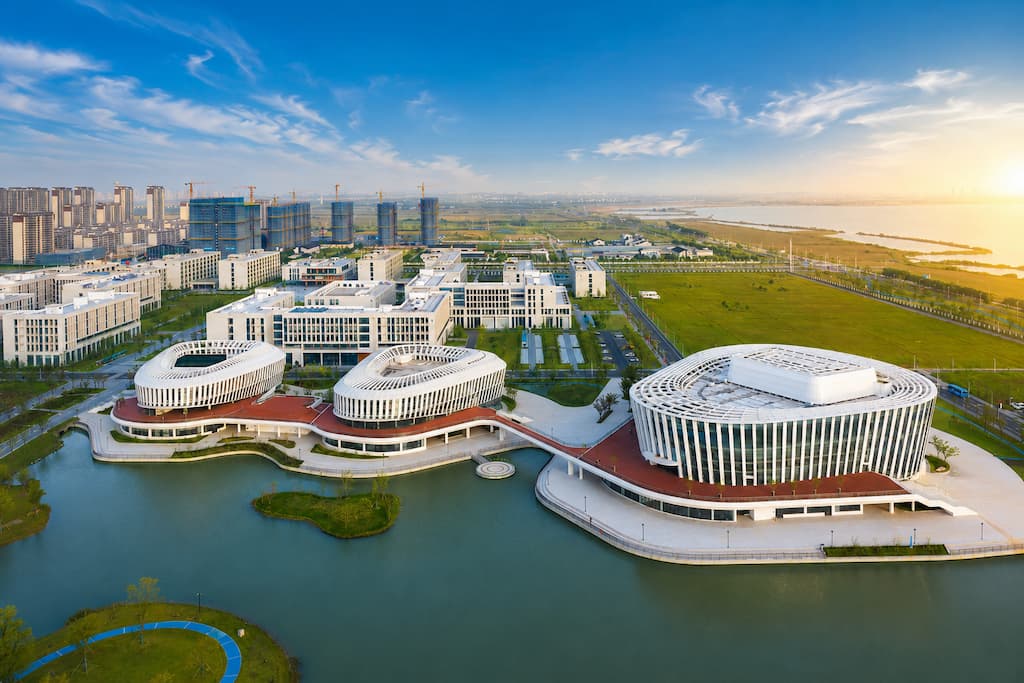 Aerial view of Hohai University's modern lakeside campus with curved white buildings beside the water at sunset