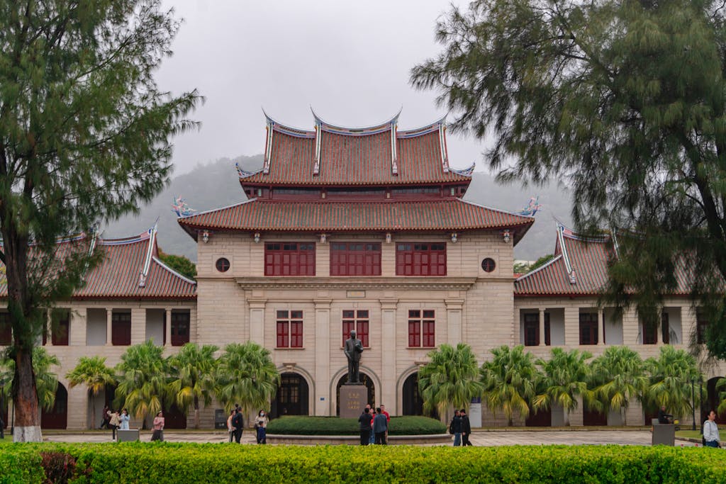 Xiamen University landmark building with Chinese tiled roofs over a Western stone facade, framed by palms and a misty mountain