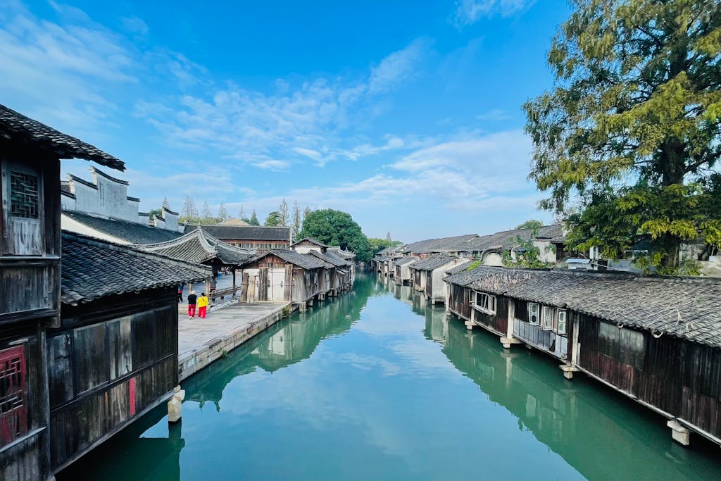 Canal lined with old wooden stilt houses and grey-tiled roofs reflected in still water at Wuzhen water town