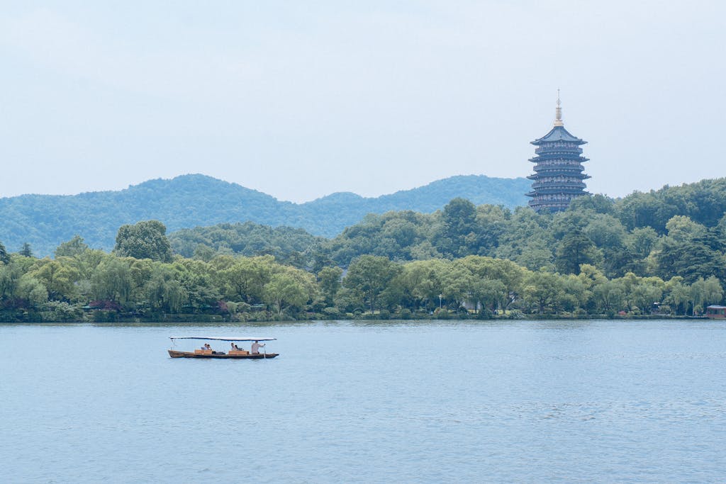 Traditional wooden boat crossing West Lake in Hangzhou with the Leifeng Pagoda above wooded hills