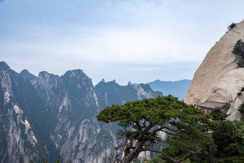 Granite peaks of Mount Hua with a pine tree and a red-roofed cliff pavilion under a blue sky