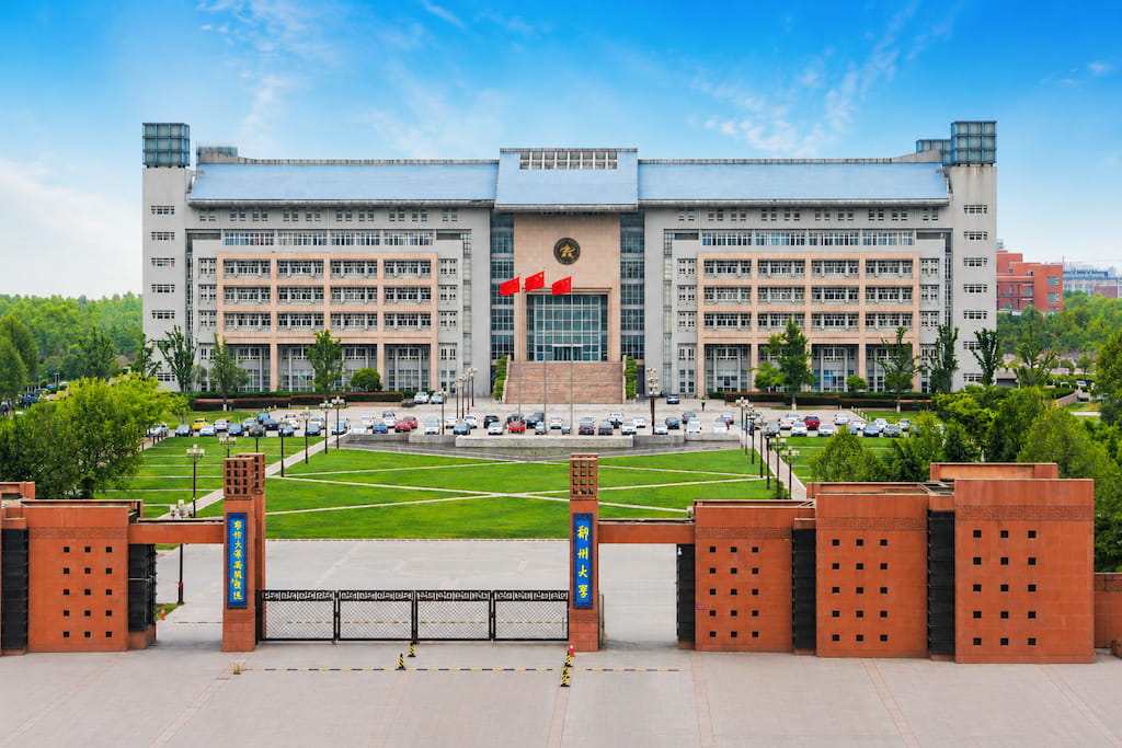 Main building and red-brick entrance gate of Zhengzhou University behind a green campus lawn