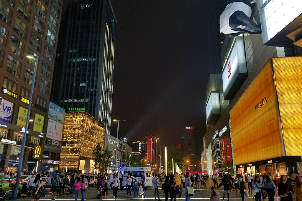 Crowds on a brightly lit Chinese city shopping street at night with skyscrapers and luxury storefronts